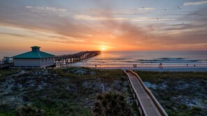 A beach with a wooden boardwalk leading to a pier.