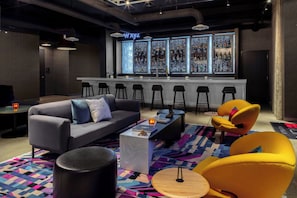 Un espace bar comprenant un comptoir, des tabourets et un coin salon avec un canapé et des fauteuils.