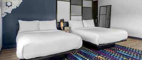 A modern hotel room with two beds, a colorful patterned rug, and a unique wall art piece.