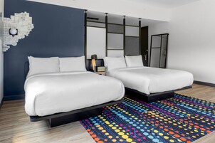 Una habitación de hotel moderna con dos camas, un tapete con estampado llamativo y una obra de arte original en la pared.