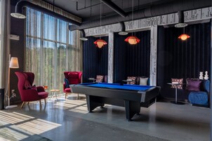 Una habitación moderna con mesa de billar, sillas rojas y un amplio ventanal con cortinas.