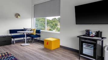Una habitación moderna con sofá, una mesita, un cofre amarillo, un refrigerador pequeño y un televisor en la pared.
