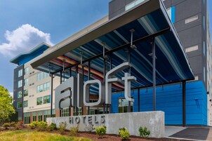 Un hotel moderno con un llamativo letrero 'aloft', grandes ventanales y fachada azul y gris.