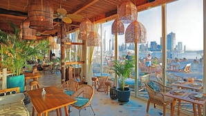 Un restaurante con amplios ventanales que ofrece vistas a la playa y al horizonte urbano.