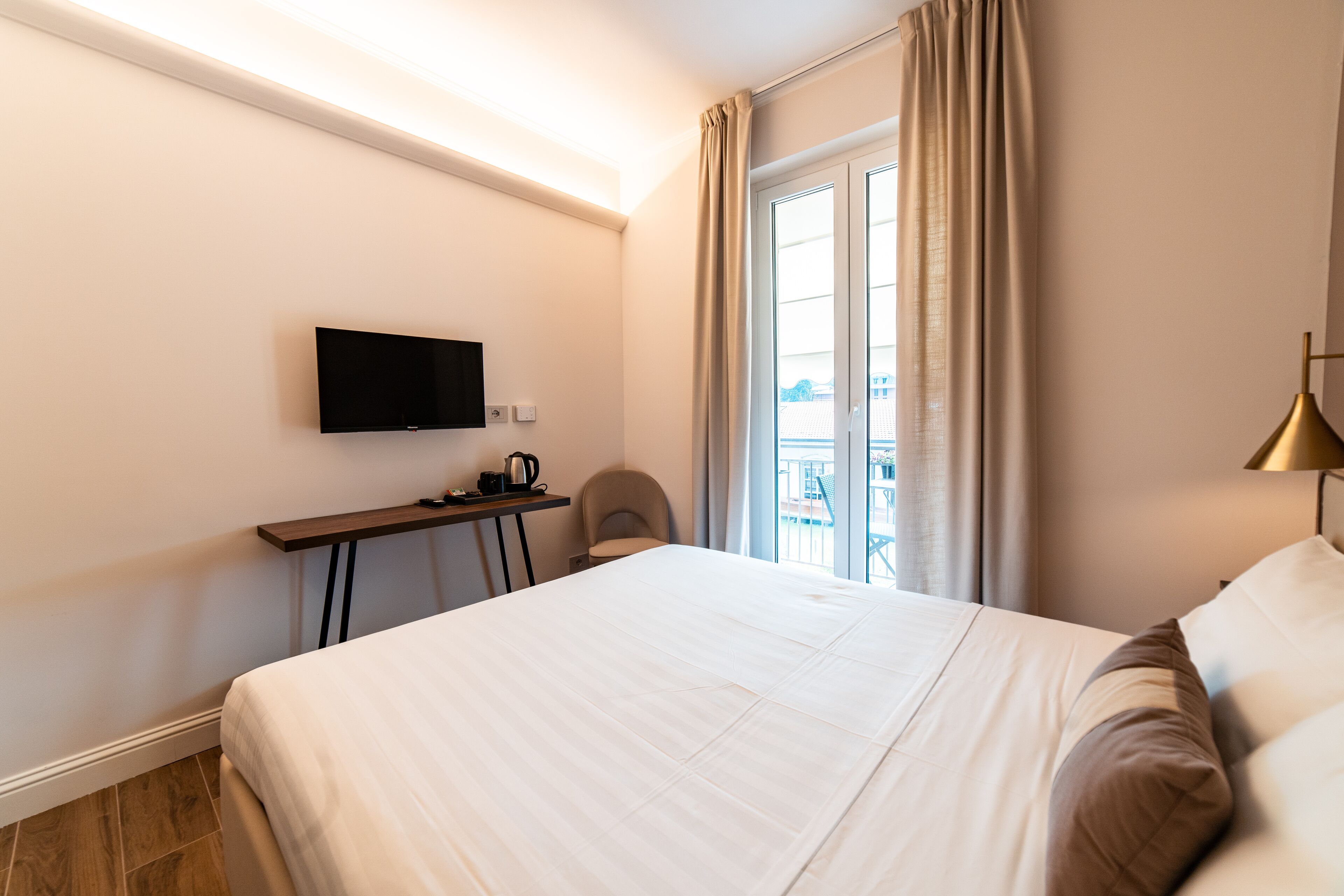 Habitació d'hotel amb un llit, un televisor fixat a la paret, escriptori amb una papereta, i vista a l'exterior per una finestra.