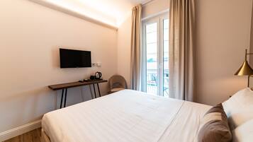 Une chambre d’hôtel avec un lit, un téléviseur fixé au mur, un bureau avec une bouilloire et une vue sur l’extérieur par une fenêtre.