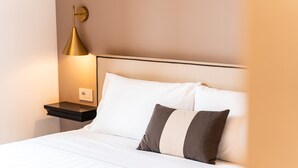 A neatly made bed with white and gray pillows, a black nightstand, and a gold lamp. - Hotel del Conte (Laveno Mombello)