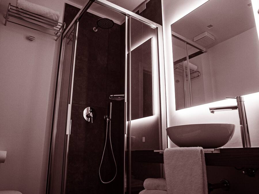 Un baño moderno con ducha de vidrio, un lavamanos con espejo y un perchero para toallas.