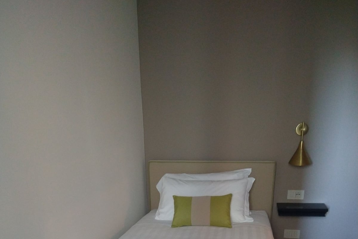 A single bed with a headboard, a bedside table, a wall-mounted lamp, and a small shelf.