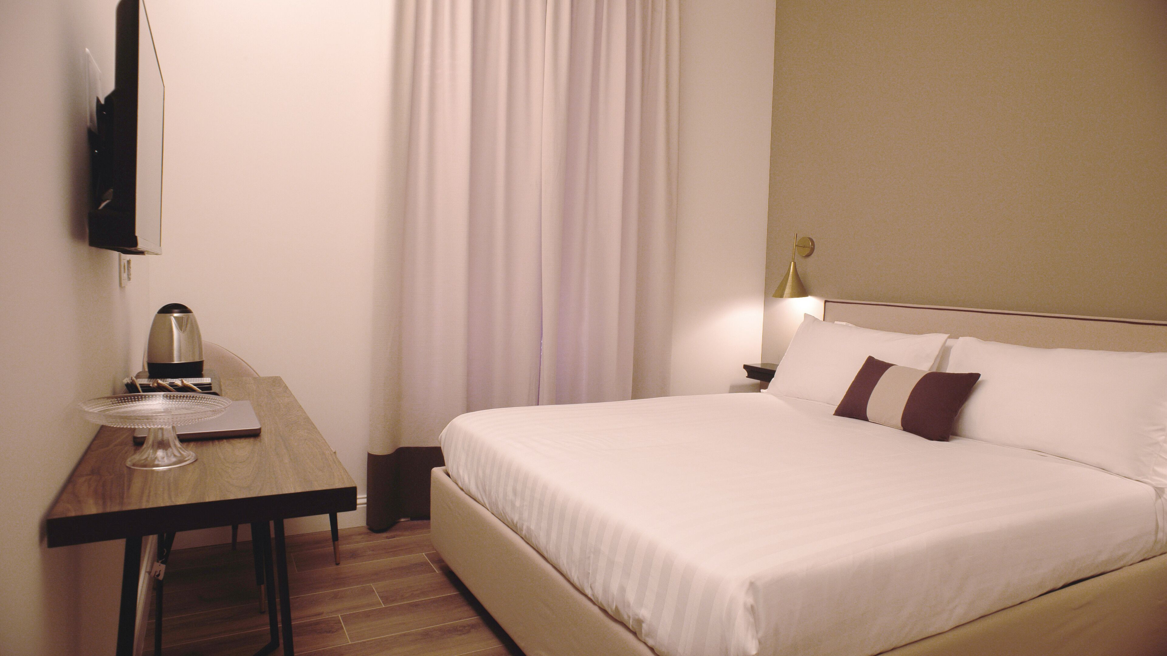 Una habitación de hotel con cama, escritorio, cafetera, lámpara y televisor.