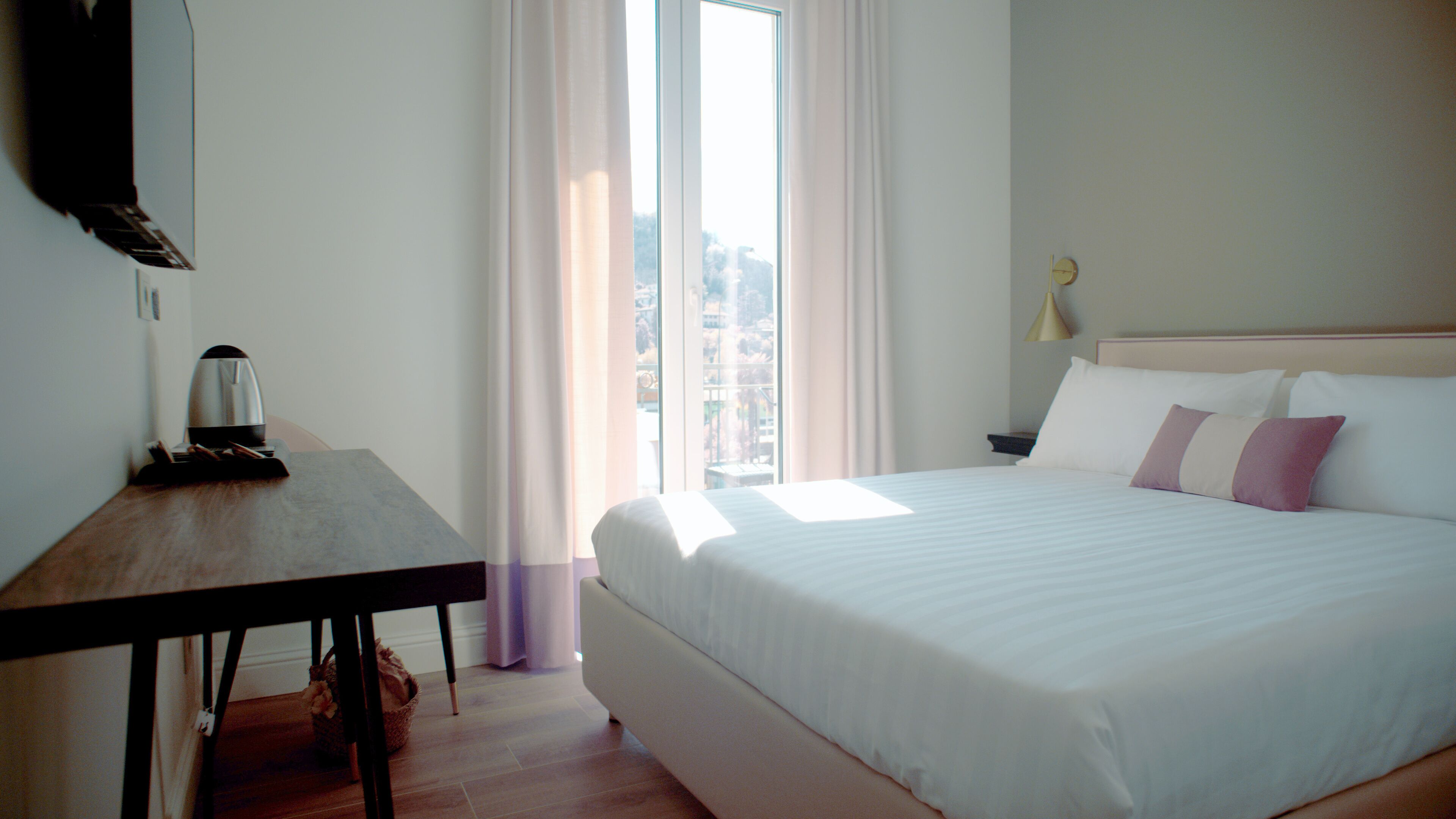 Una habitación de hotel con cama, escritorio, lámpara y ventana con cortinas.