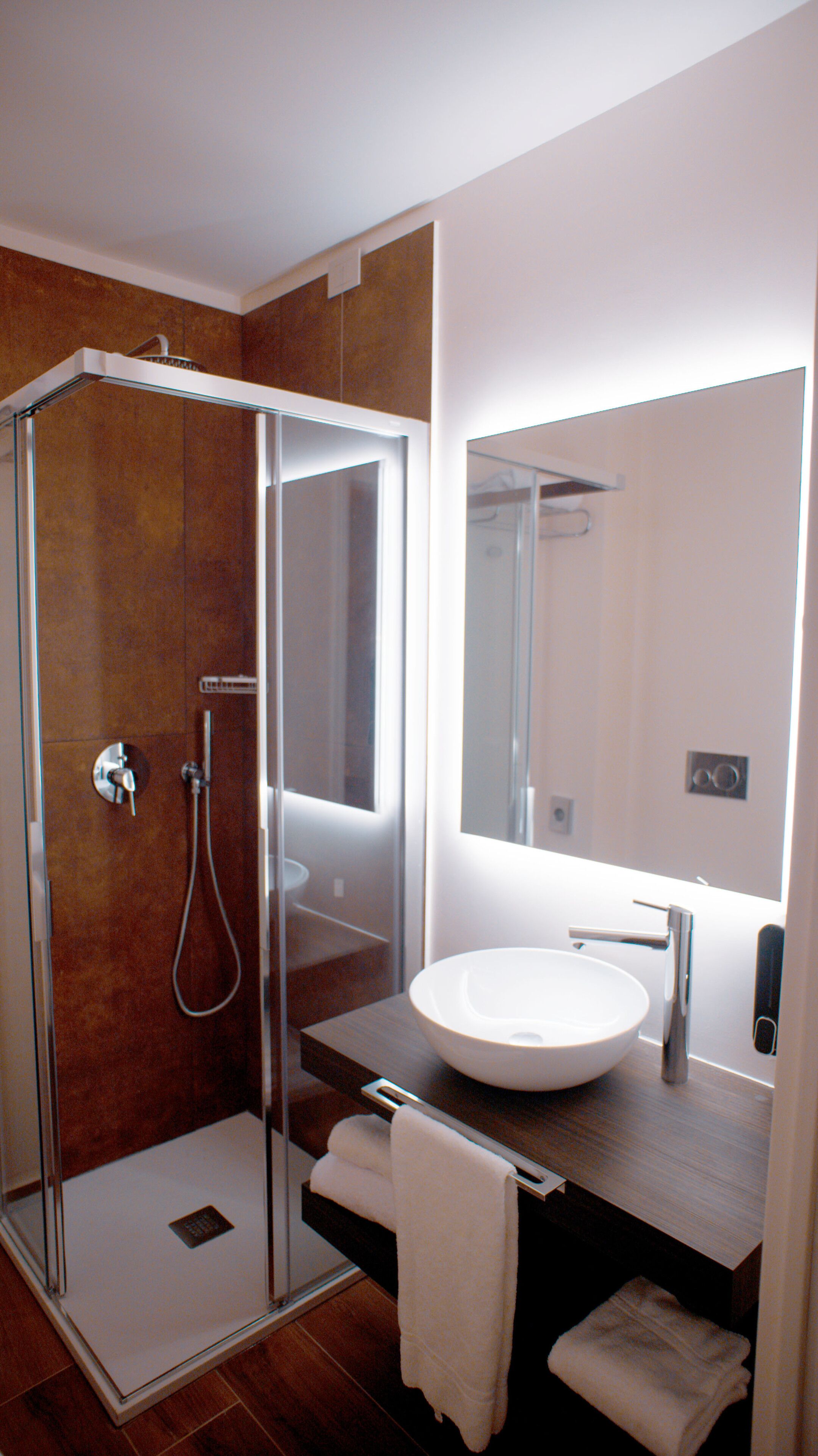 Een moderne badkamer met een douchecabine van glas, een witte wastafel en een grote spiegel boven het aanrecht.