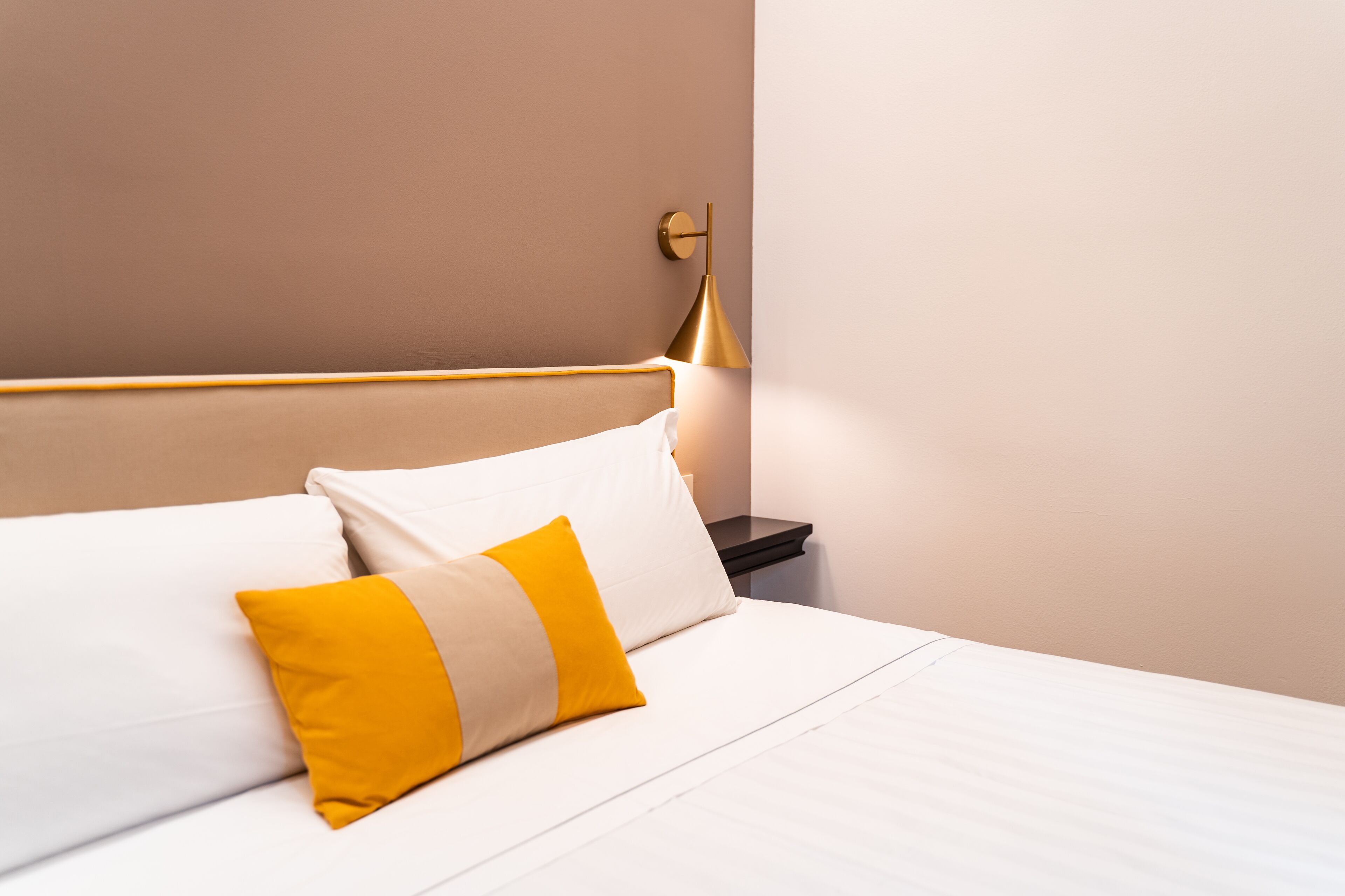 A neatly made bed with white and yellow pillows, a gold-colored headboard, and a bedside lamp on a nightstand.