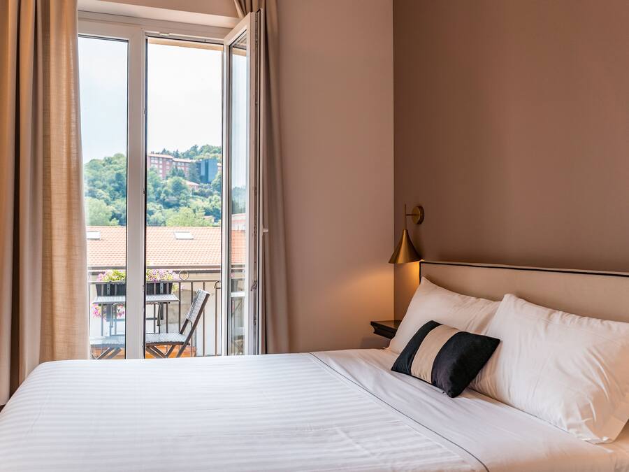 Et hotelværelse med en stor seng, et sengebord, en lampe og udsigt til en balkon med havemøbler.