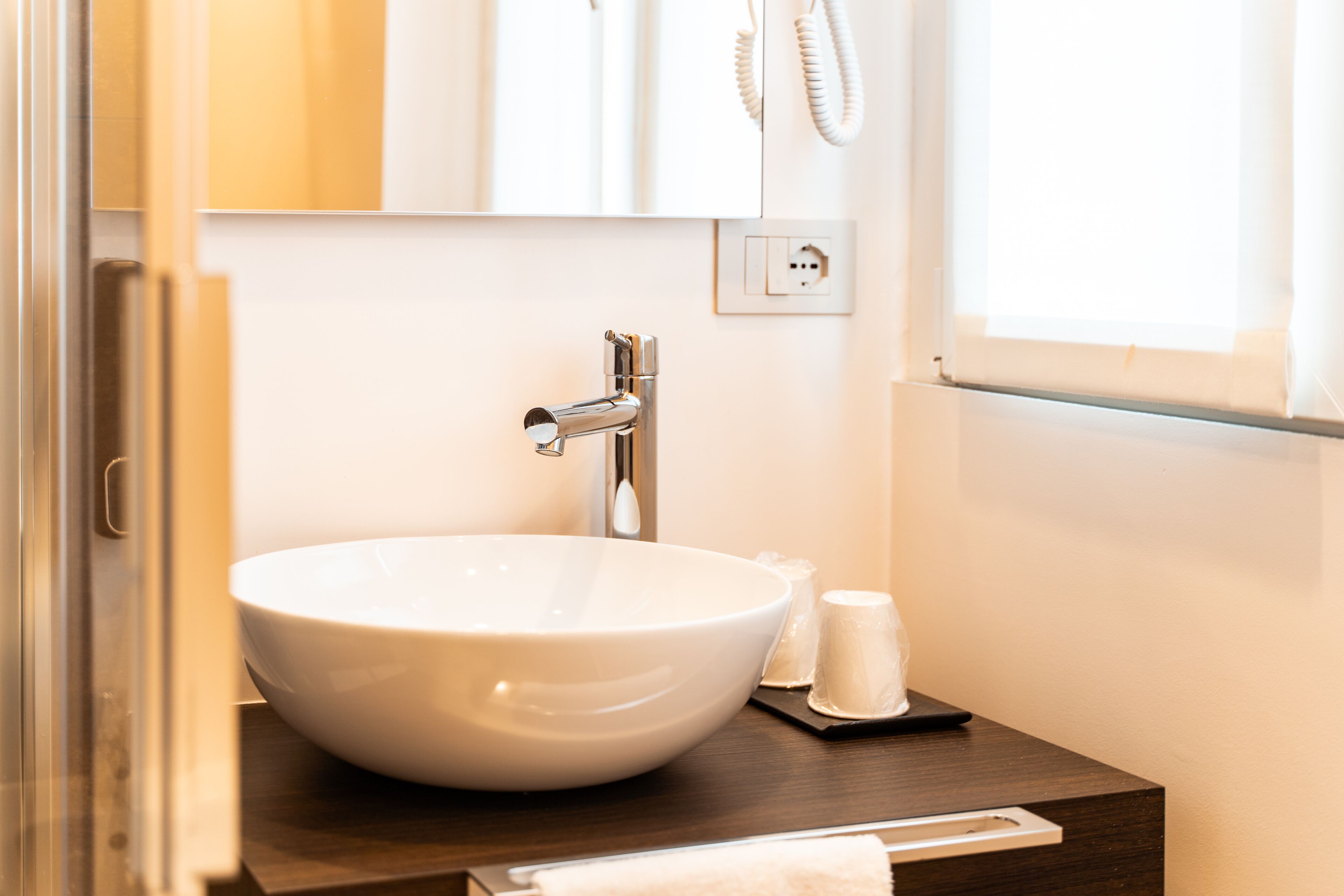Un évier en céramique blanche, doté d’un robinet moderne, d’un petit porte-savon et d’une serviette, est posé sur un plan de travail en bois dans une salle de bain.