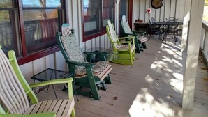 Eine überdachte Veranda mit grünen Adirondack-Stühlen, einem Tisch und einer Wanduhr.