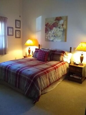 A bedroom with a large bed, two bedside tables with lamps, a painting on the wall, and a window with curtains.