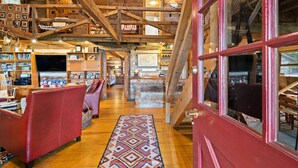 A cozy, rustic interior with wooden beams, a red door, and a central staircase.