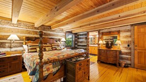 A log cabin bedroom with a wooden bed, a dresser, and a mirror.