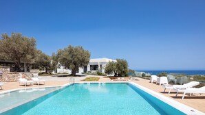 A pool with lounge chairs, a stone wall, and a view of the sea. - 100m2 heated pool, absolute privacy and mesmerising views! (Rethymno)