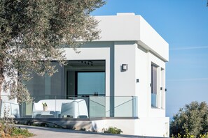 Une maison moderne à deux étages, dotée d’un balcon, de grandes fenêtres et d’un design minimaliste.