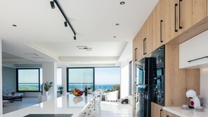 A modern kitchen with a large island, wooden cabinets, and a view of the ocean. - 100m2 heated pool, absolute privacy and mesmerising views! (Rethymno)