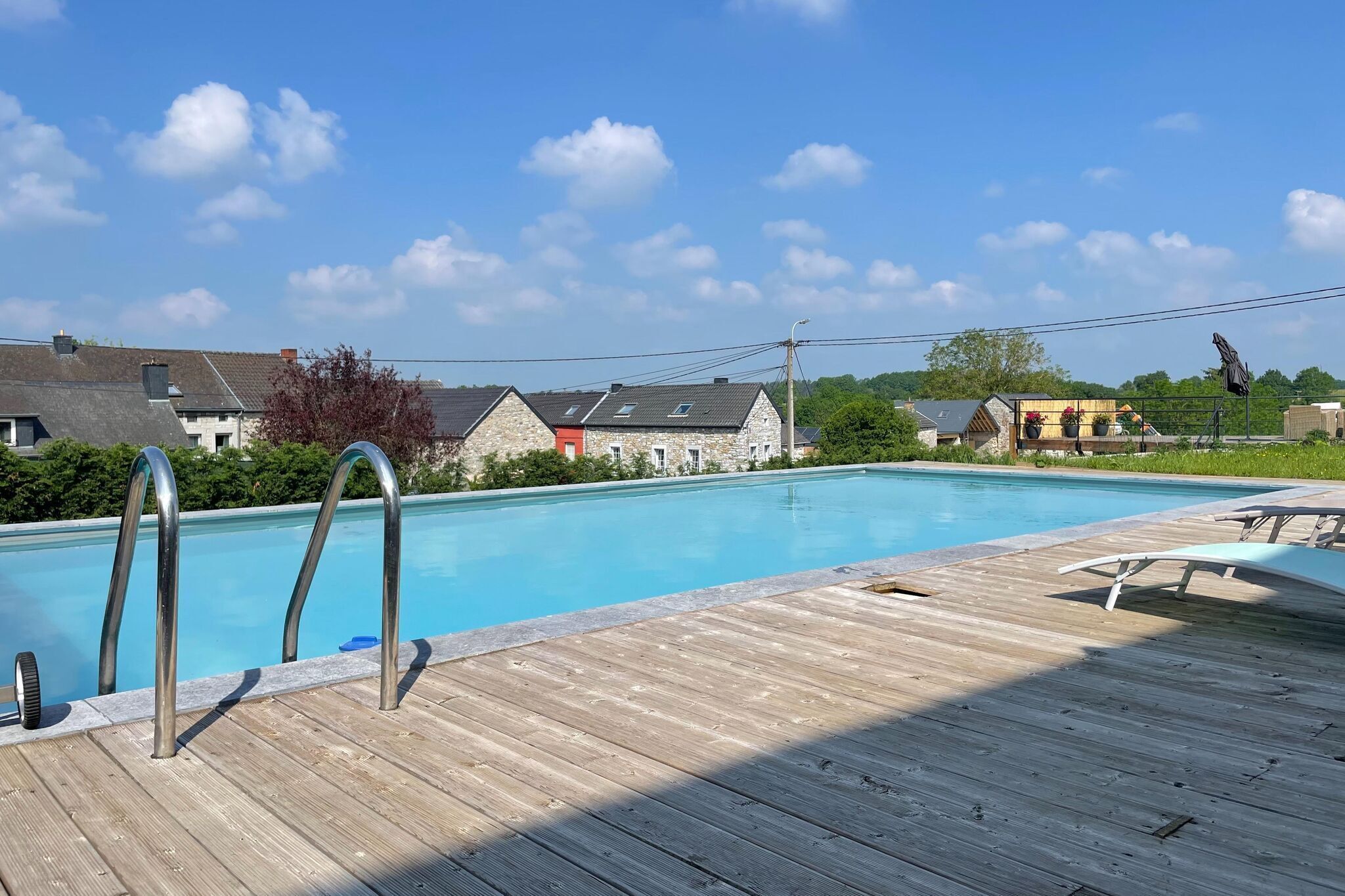 Eine Holzterrasse mit Swimmingpool, Metallleiter und Liegestühlen.
