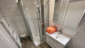 Un baño moderno con cabina de ducha de vidrio, un lavabo blanco y un inodoro pequeño.