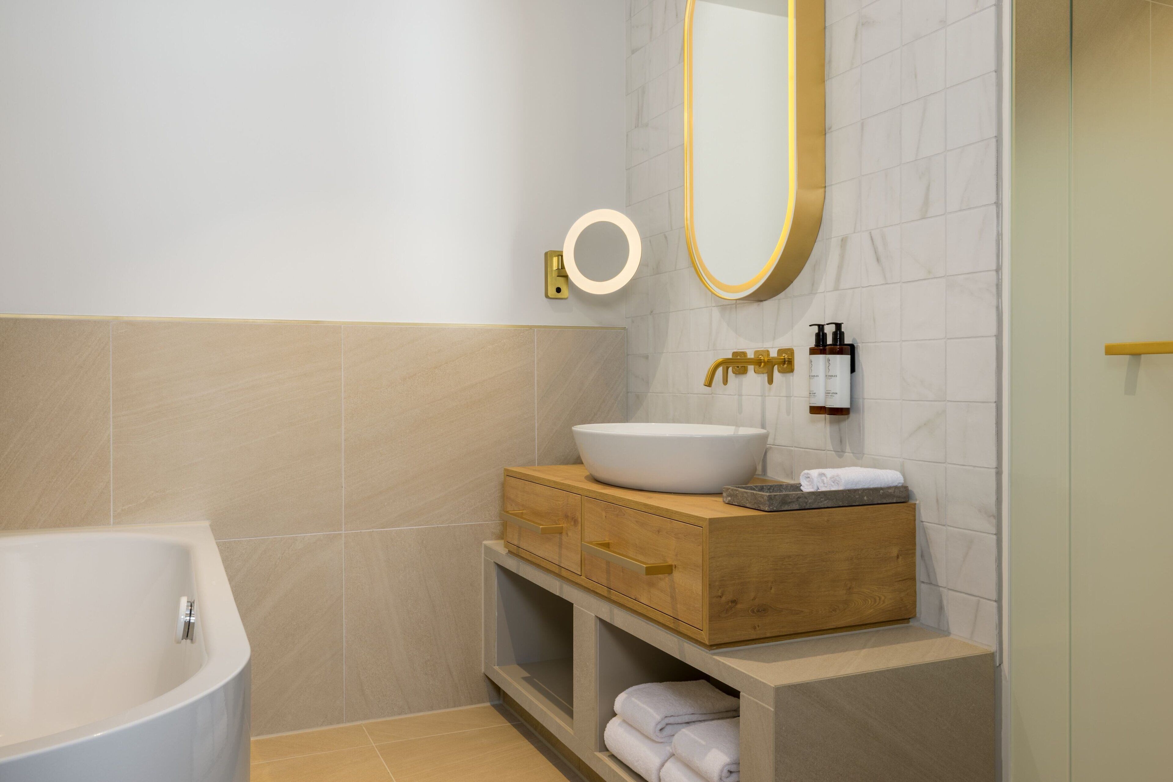 Un baño moderno con una bañera independiente, un tocador de madera con un lavamanos grande y un espejo con marco dorado.