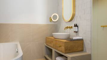 Un baño moderno con una bañera independiente, un tocador de madera con un lavamanos grande y un espejo con marco dorado.