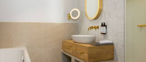 A modern bathroom with a freestanding bathtub, a wooden vanity with a large sink, and a mirror with a gold frame.