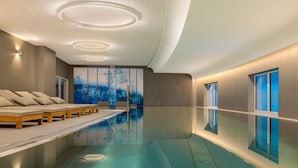 A modern indoor swimming pool with a seating area, a large wall mural, and a ceiling with circular light fixtures. - A-ROSA Tegernsee (Tegernsee)