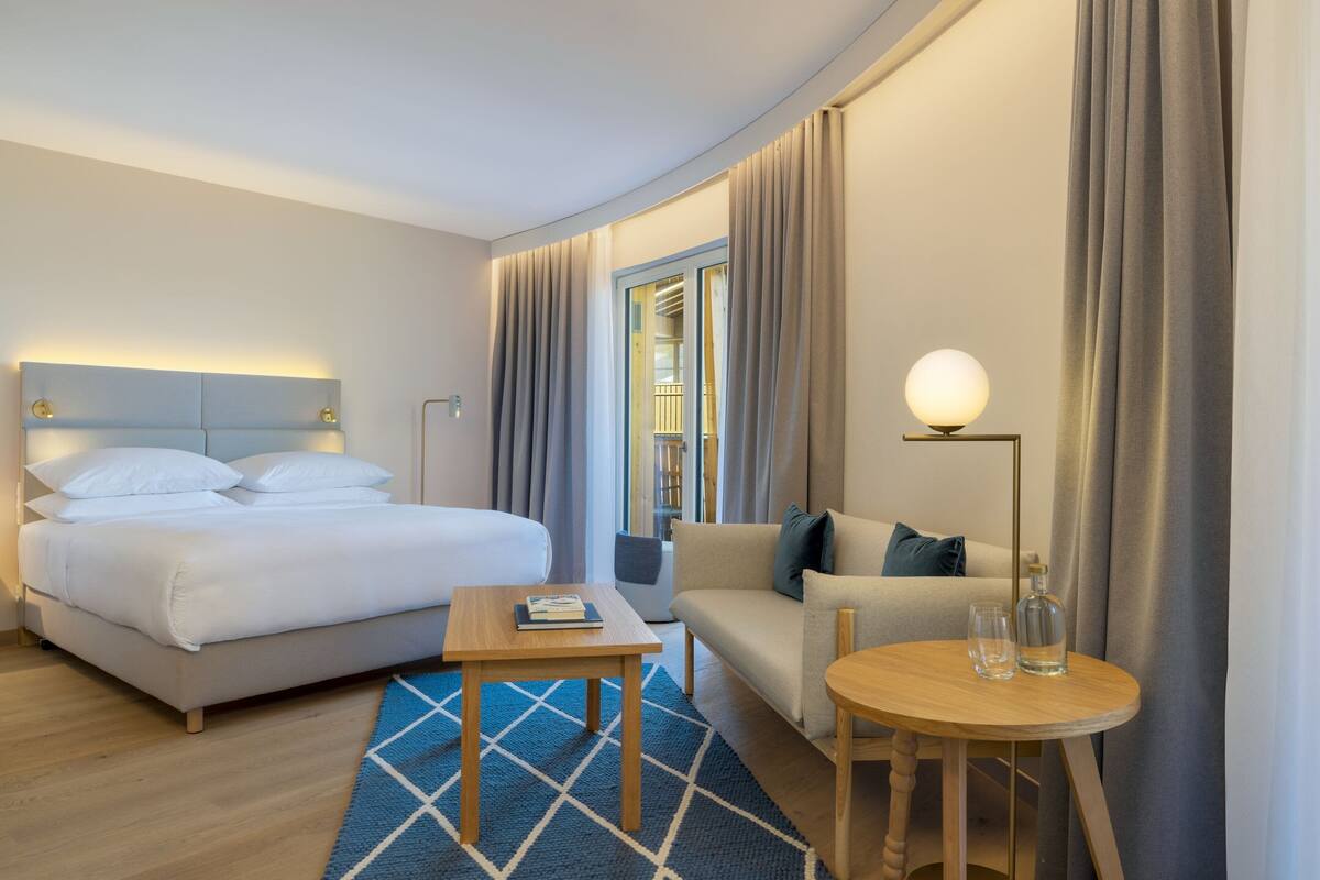 A hotel room with a bed, a sofa, a small table, and a lamp.
