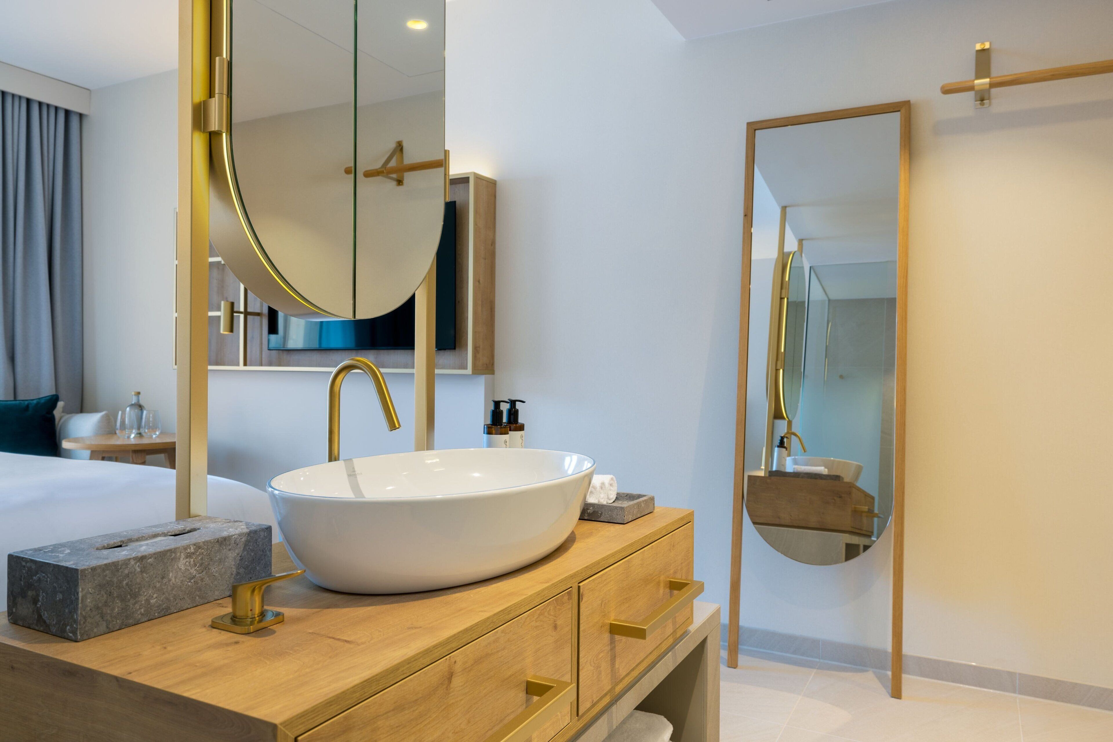 A modern bathroom with a large oval sink, gold faucets, and a wooden vanity.
