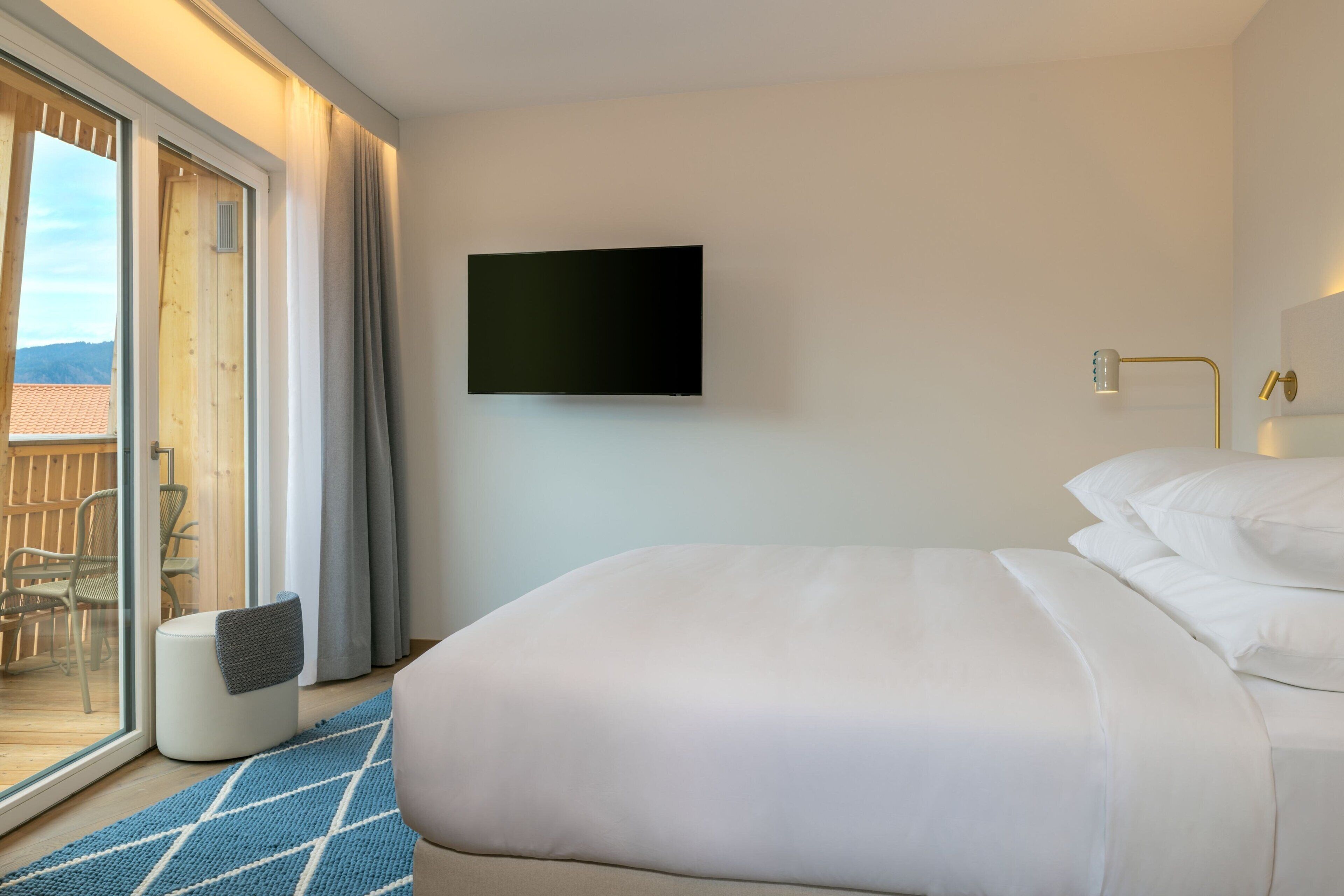 A hotel room with a bed, a television mounted on the wall, and a view of the outdoors through a sliding glass door.