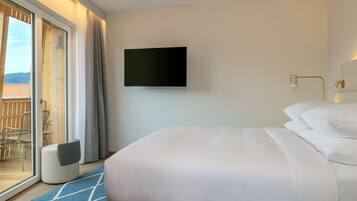 Habitación de hotel con cama, televisor montado en la pared y vistas al exterior a través de una puerta corrediza de vidrio.