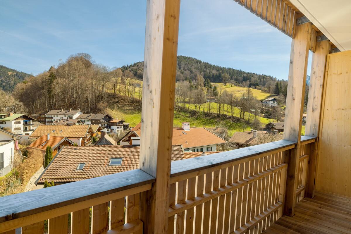 A wooden balcony overlooking a residential area with houses and hills in the background.