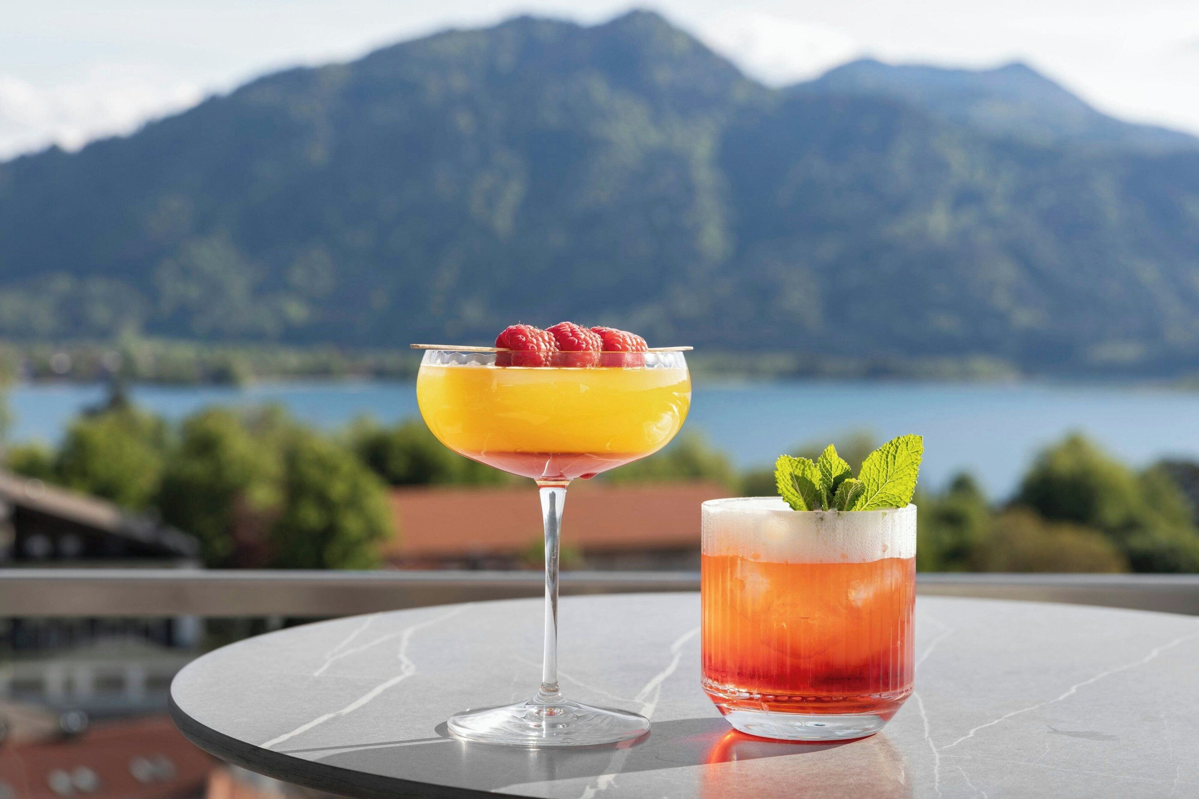Two cocktails on a table with a mountain view in the background.
