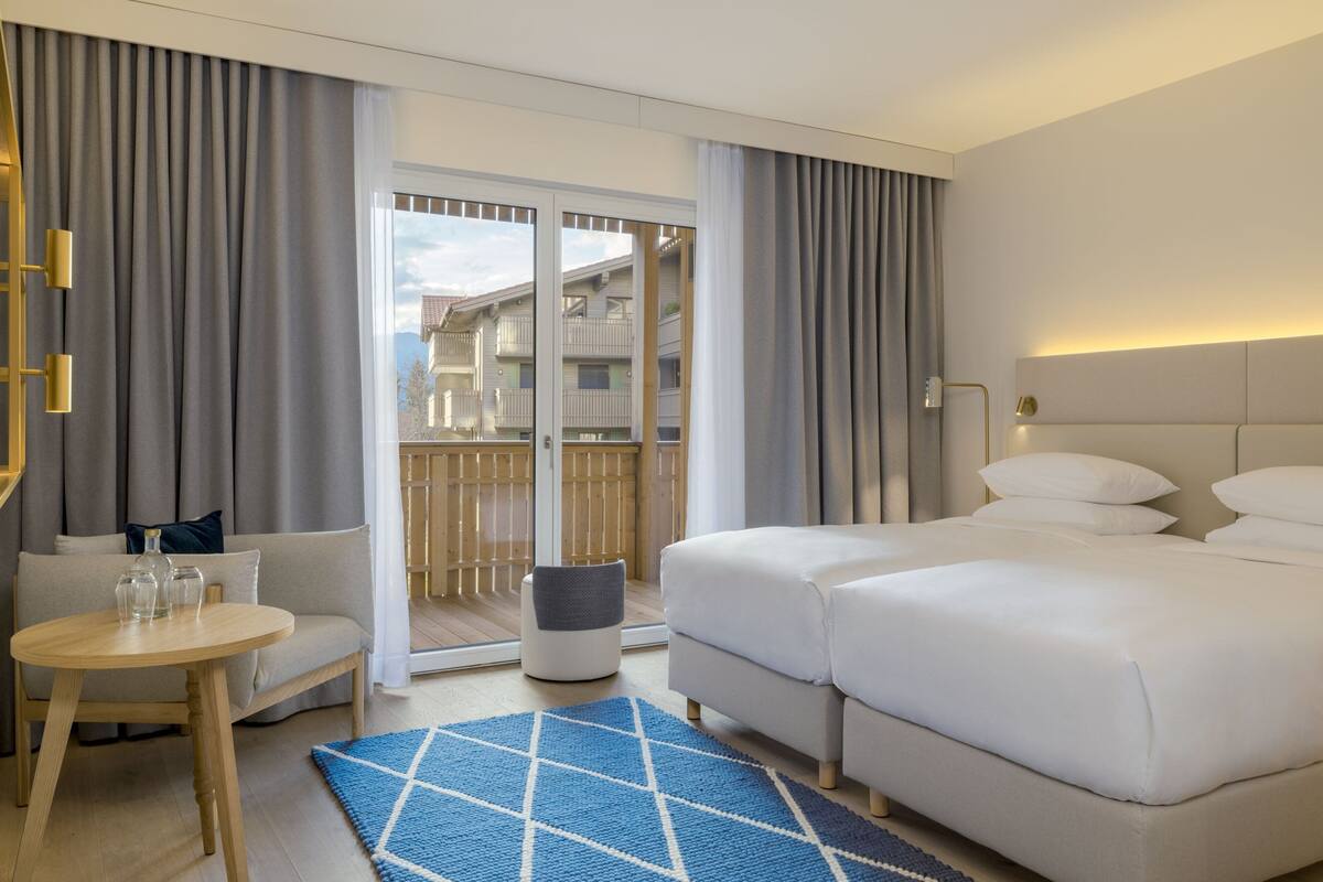 A hotel room with a large bed, a sofa, a small table, and a view of the outside balcony.