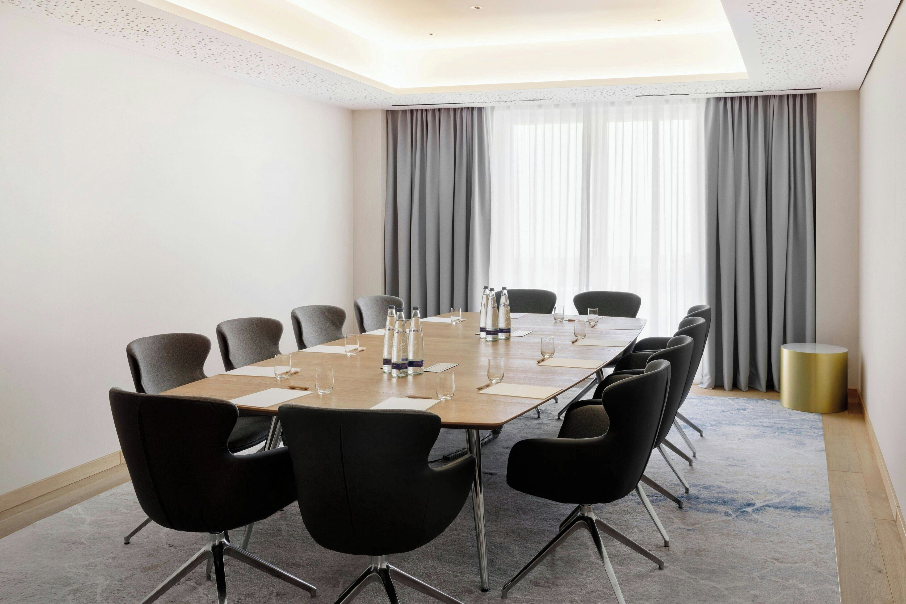 A conference room with a long table, black chairs, and a carpeted floor.