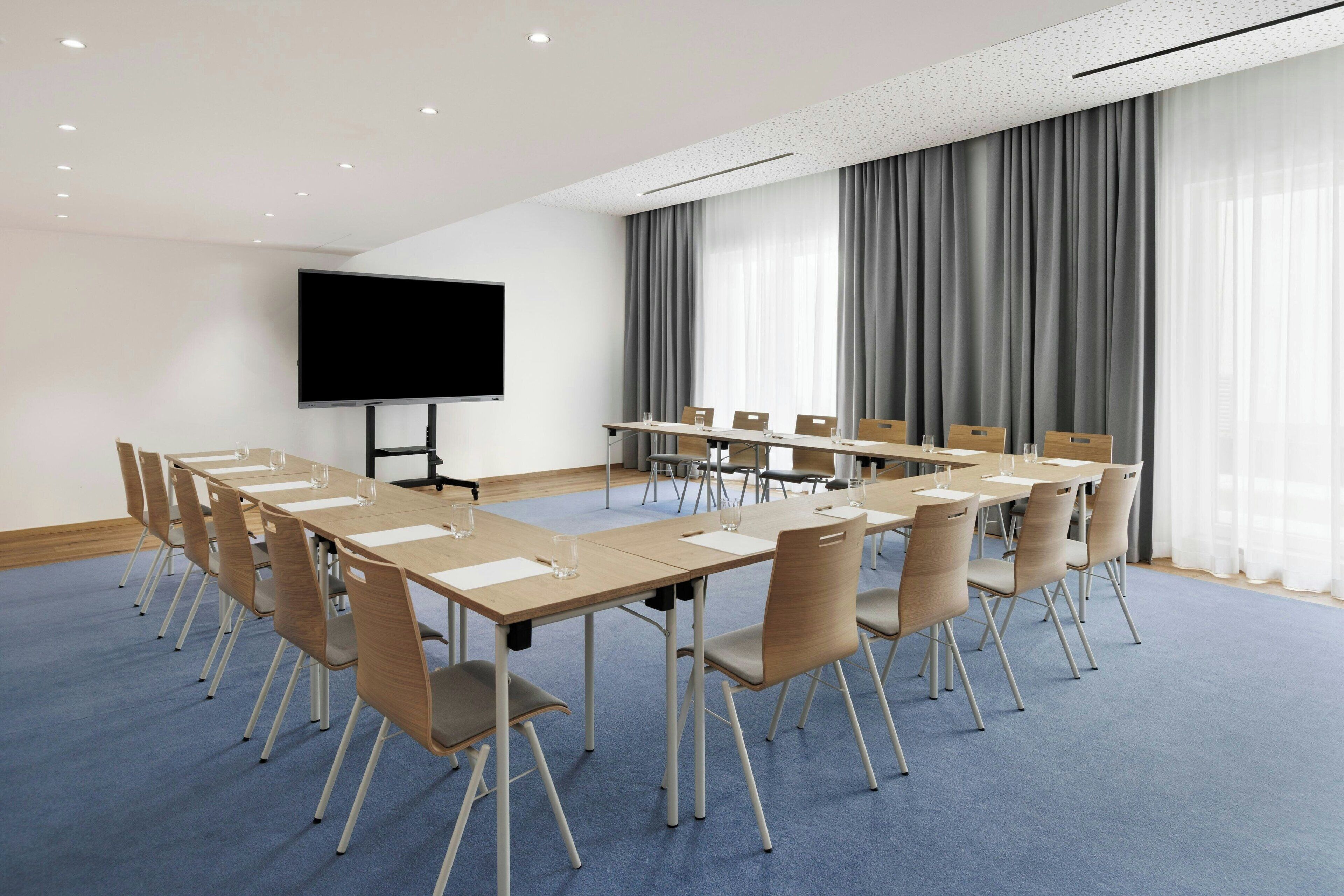 A conference room with a long table, chairs, a flat-screen TV, and a large window with curtains.