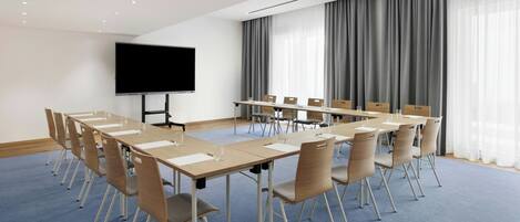 A conference room with a long table, chairs, a flat-screen TV, and a large window with curtains.