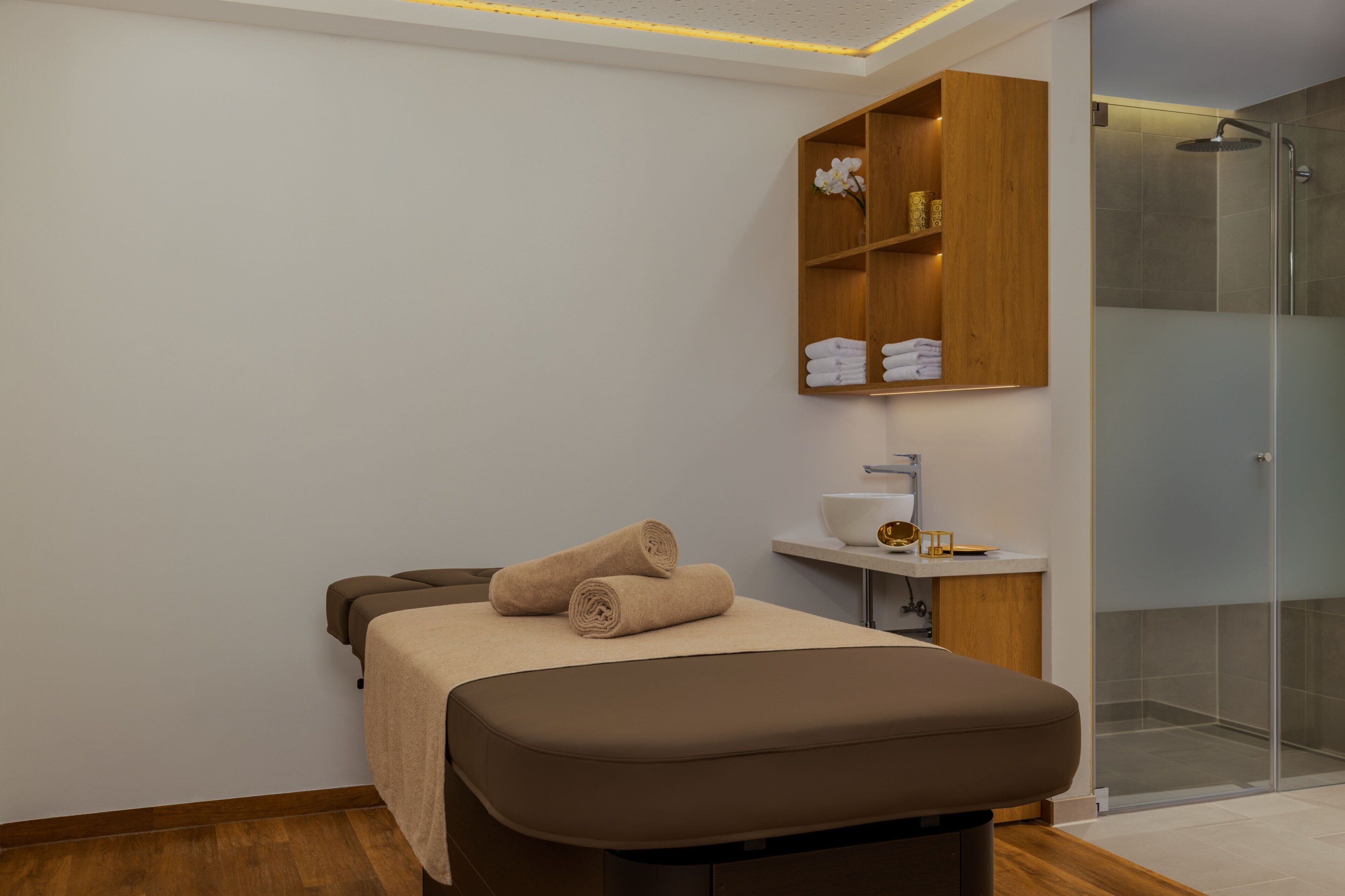 A modern bathroom with a glass shower, a wooden vanity, and a bed with towels.