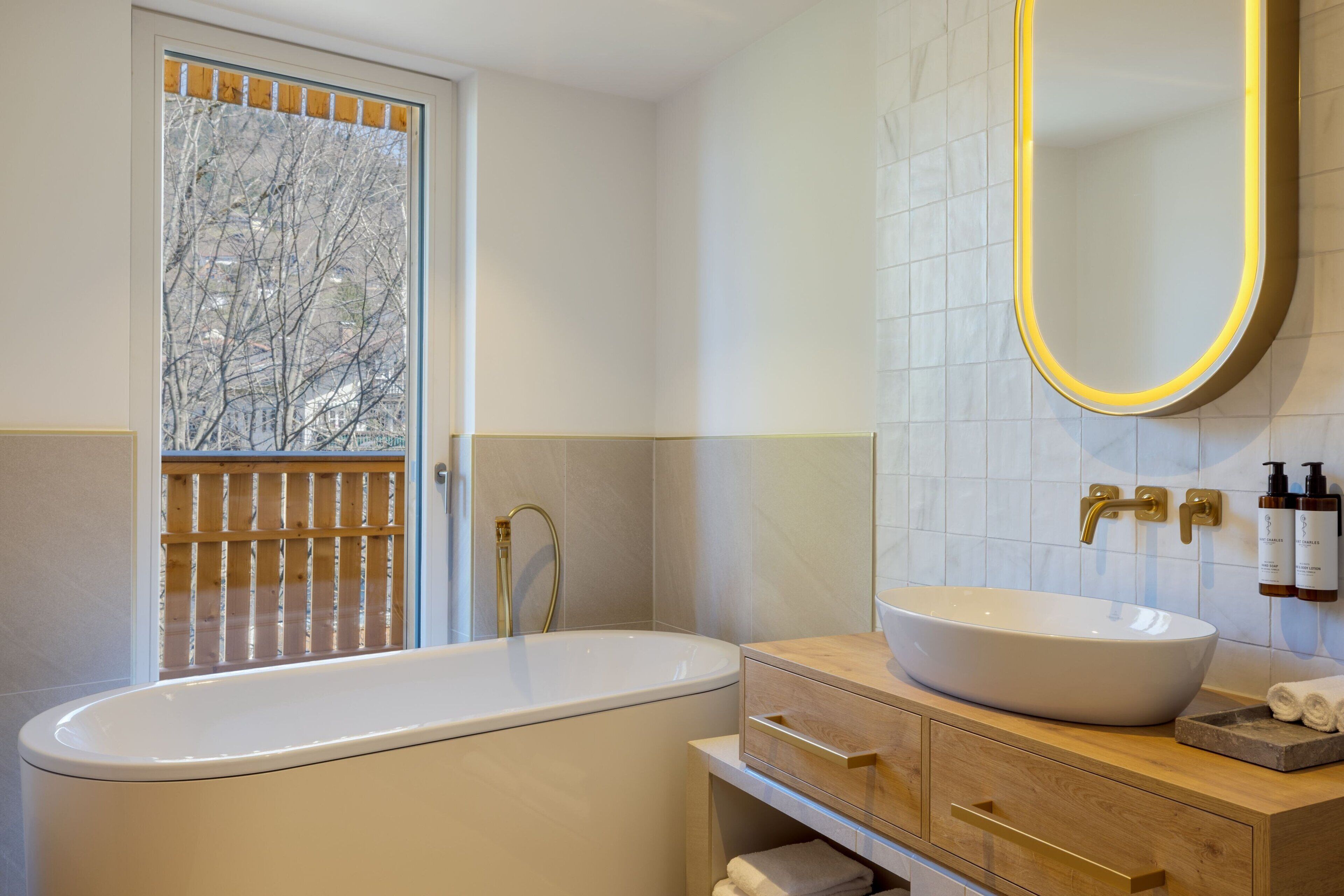 Un baño moderno con una bañera independiente, un espejo grande y un tocador de madera con lavabo.