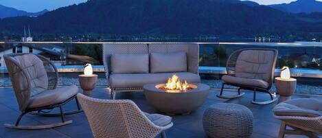 Una terraza con mobiliario de mimbre, una chimenea y vistas a las montañas.