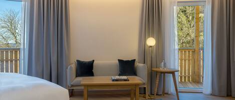 Habitación de hotel con cama, sofá, mesa de centro, lámpara y vistas a una terraza de madera.