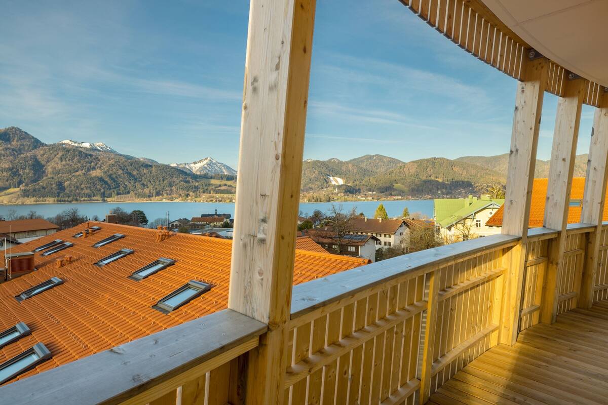 A wooden balcony with a view of a lake and mountains.