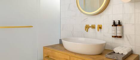 A bathroom with a white sink, gold fixtures, and a marble-tiled wall.