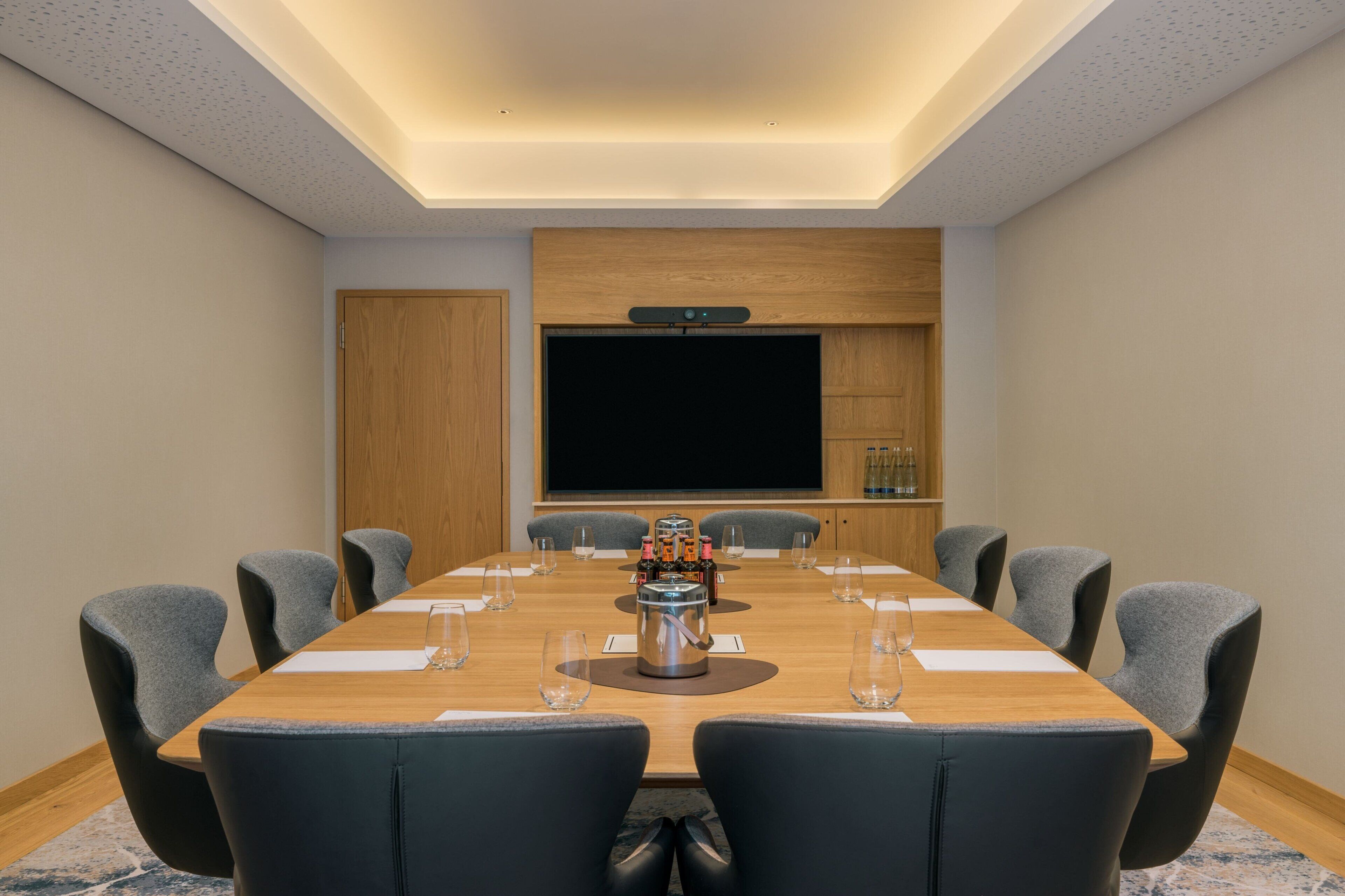 Uma sala de conferências com uma mesa comprida, cadeiras, uma máquina de café e uma tela grande.