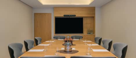 Uma sala de conferências com uma mesa comprida, cadeiras, uma máquina de café e uma tela grande.